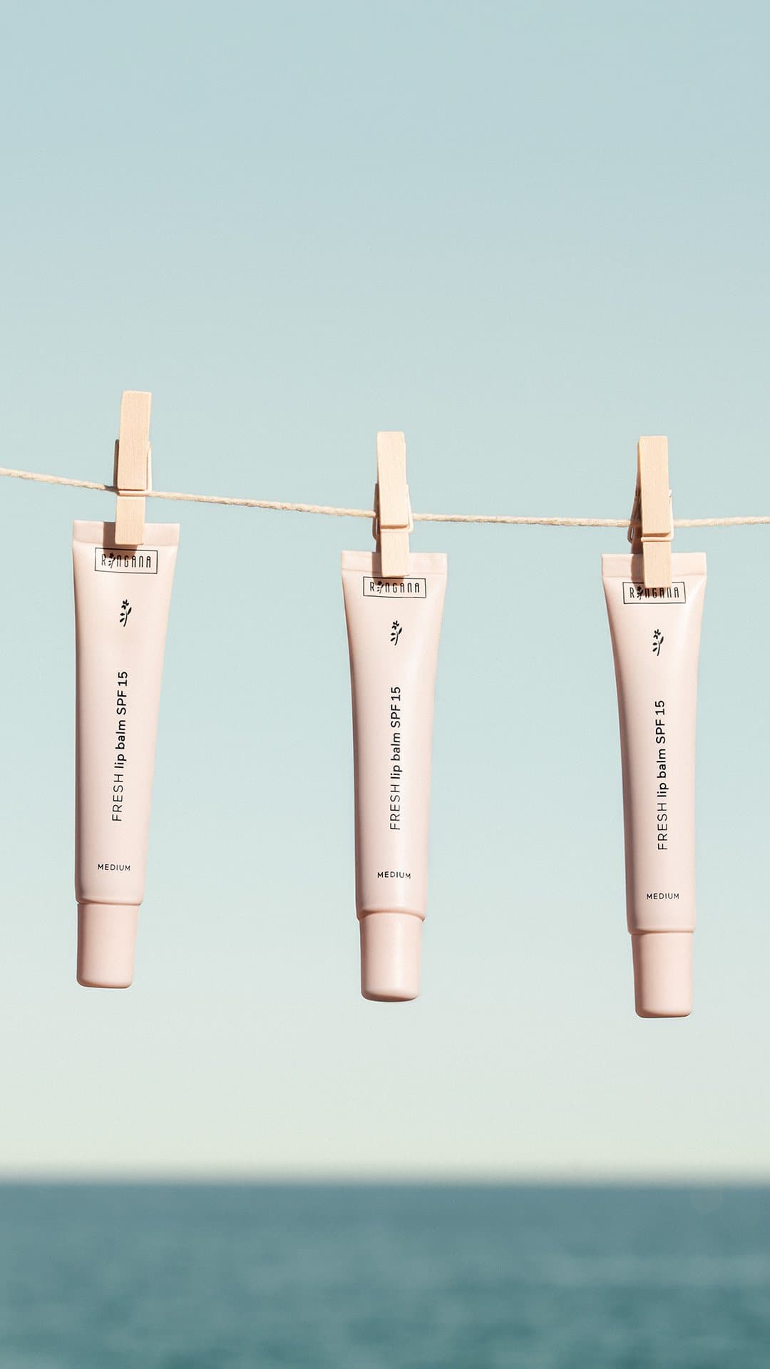 Three tubes of Ringana FRESH lip balm SPF 15 hanging on a line over the sea