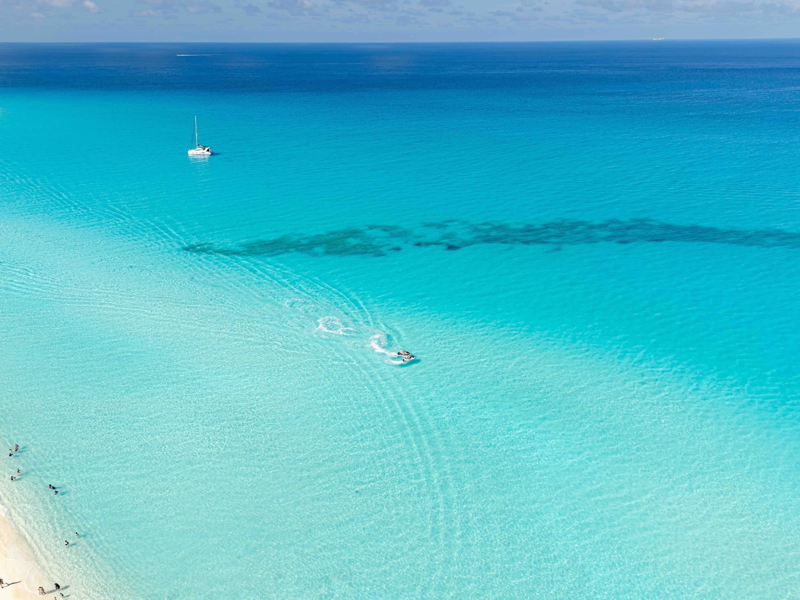 Turquoise Caribbean water from above, with a sailboat on the shallows